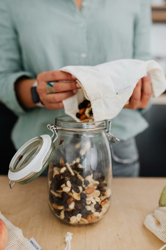 Close-up of a woman pouring homemade trail mix into a glass jar, promoting a zero-waste lifestyle.